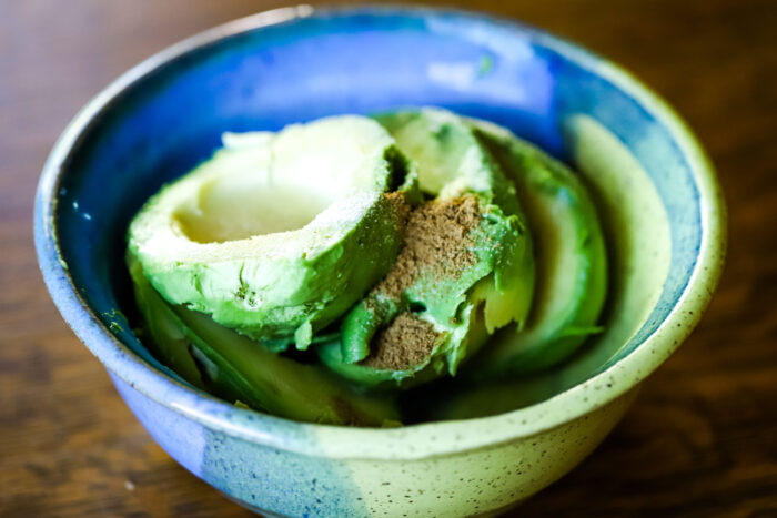 ripe avocadoes in bowl with ingredients for recipe