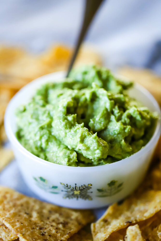 guacamole in a bowl with spoon and surrounded by tortilla chips