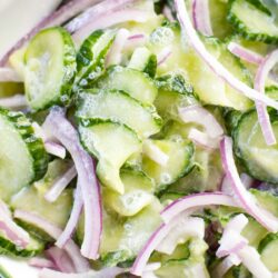 close up of german cucumber salad in bowl with spoon