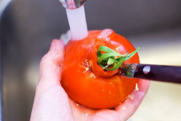 tomato under running water being cored with knife