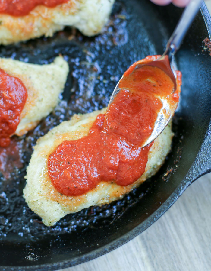 sauce spooned onto parmesan chicken in cast iron pan