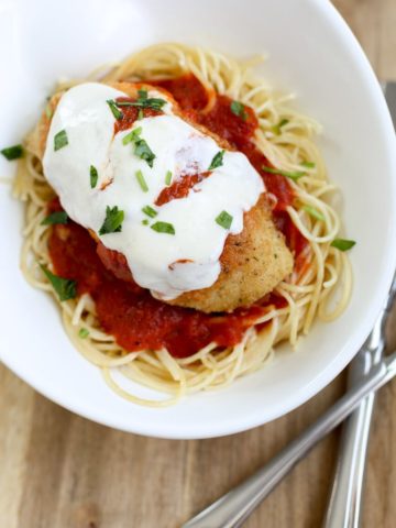 plate of baked chicken parmesan on top of noodles