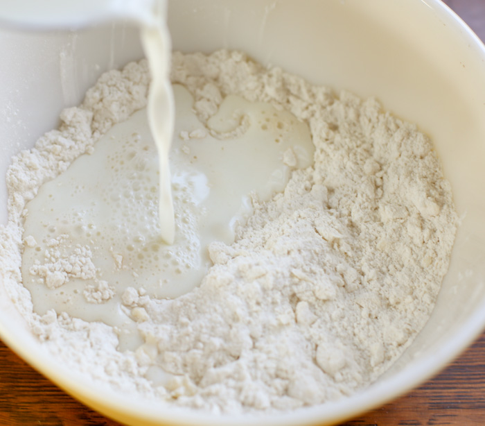 pouring milk into homemade biscuit ingredients