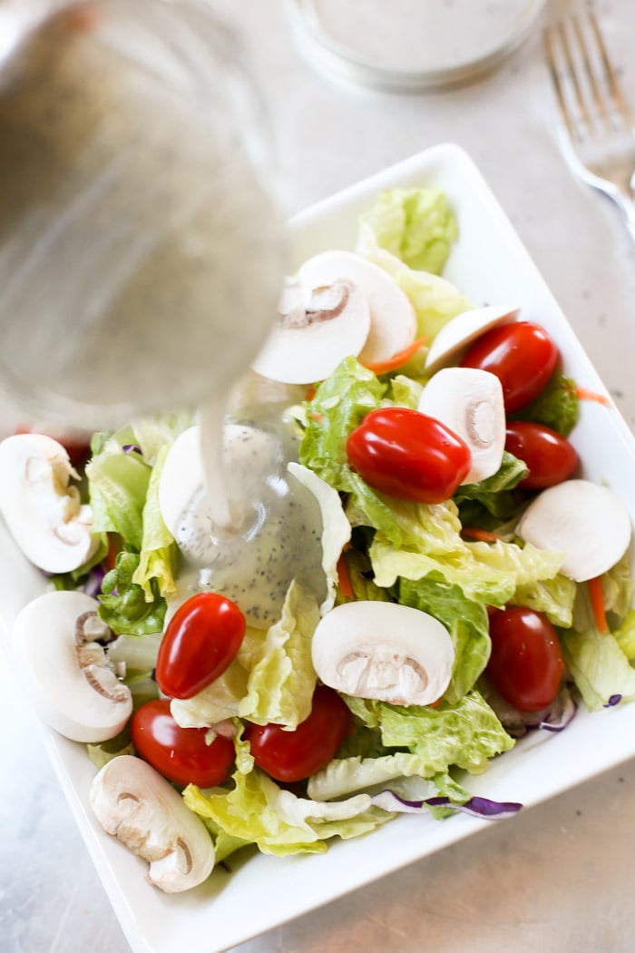 pouring poppyseed dressing on salad in bowl