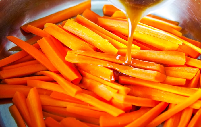 pouring maple syrup on chopped carrots