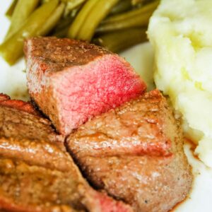 sliced venison on plate with mashed potatoes and green beans