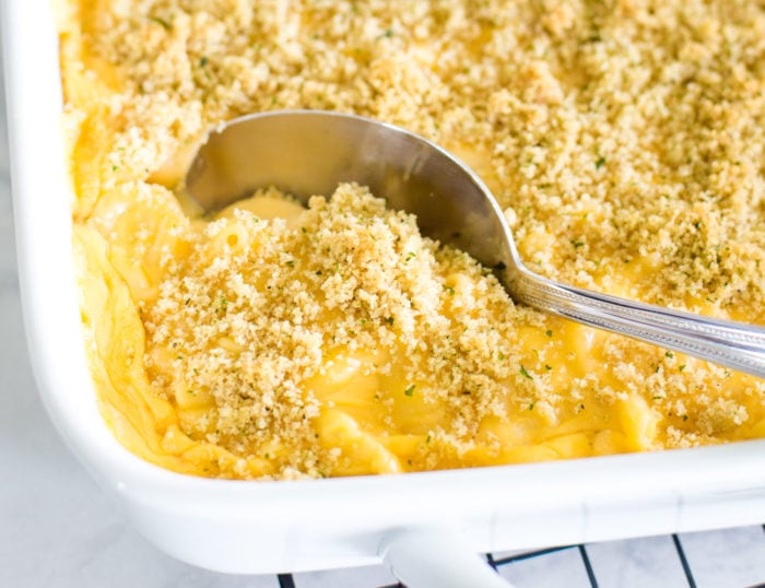 scooping out mac and cheese from baking dish
