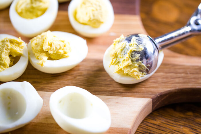 filling each egg white with yolk mixture using cookie scoop