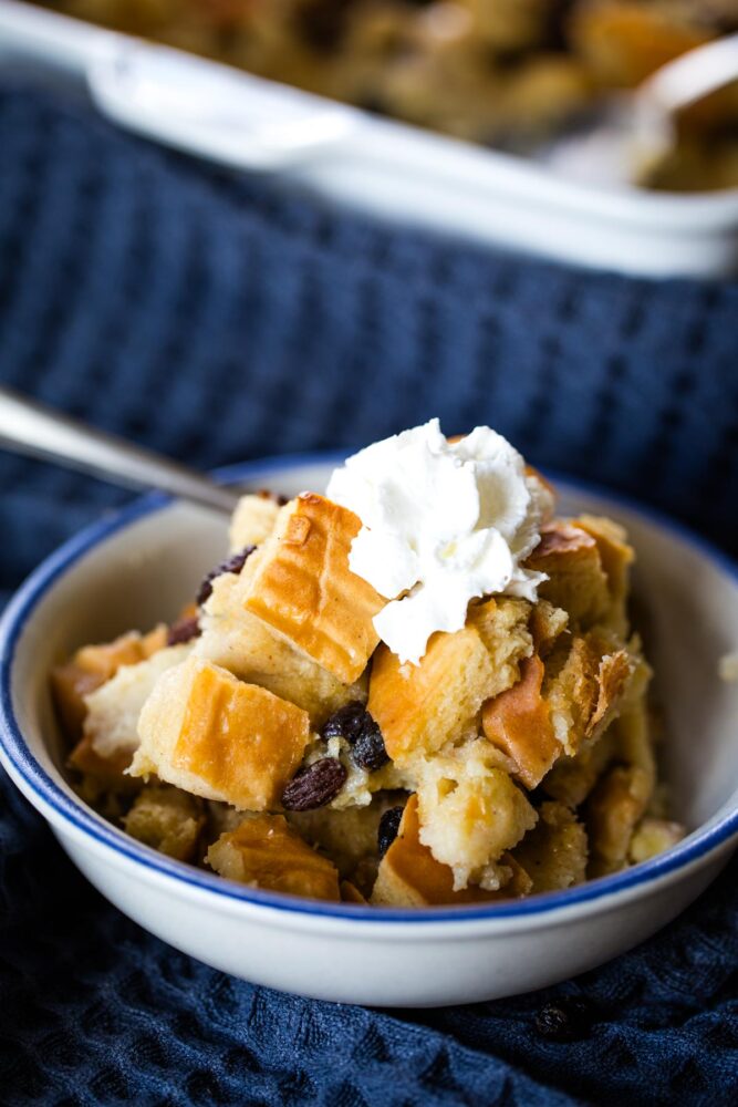 bread pudding in bowl with spoon topped with whipped cream