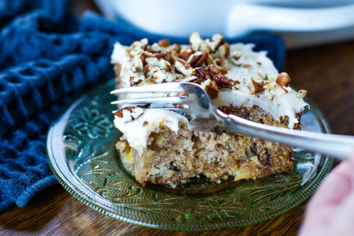 fork slicing into piece of hummingbird cake on plate with fork