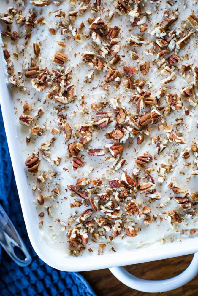 cream cheese frosting on cake topped with pecans