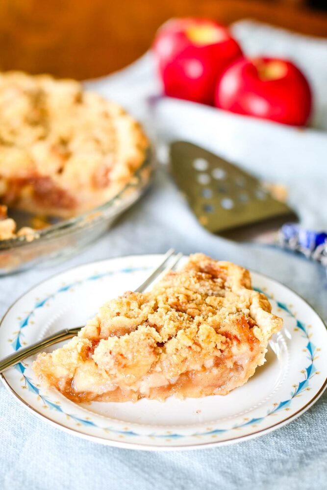 slice of pie with pie cutter apples and whole pie on table