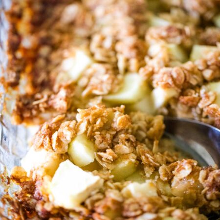 close up of apple pudding with serving spoon in baking dish