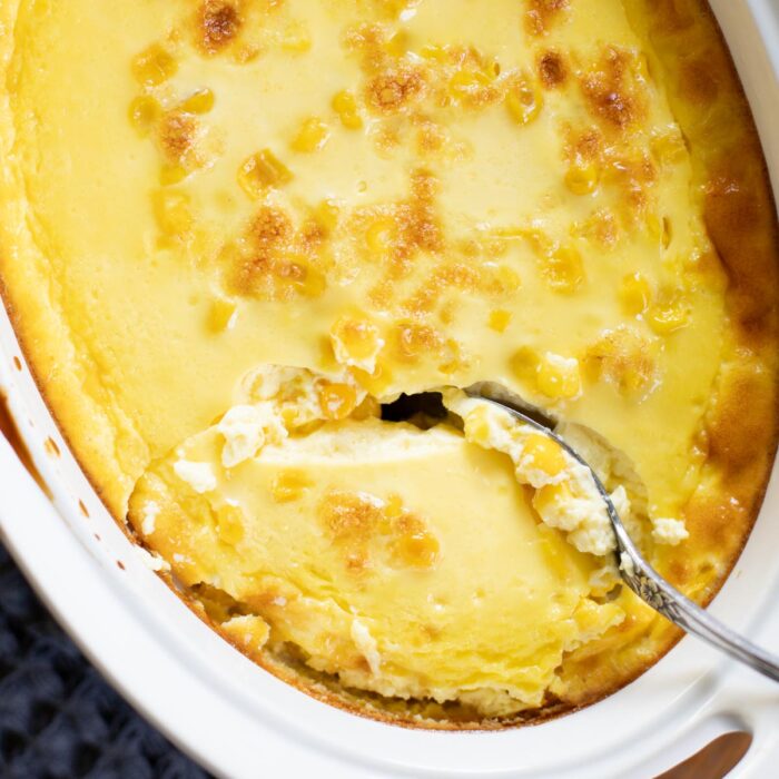 serving of corn pudding being scoop out of baking dish