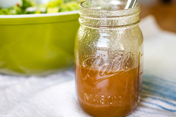 sweet and sour dressing in mason jar beside salad bowl