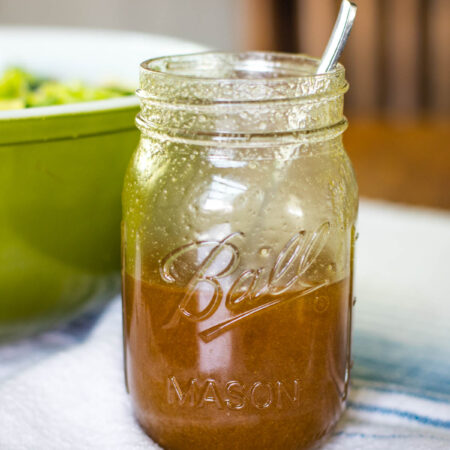 sweet and sour dressing in pint jar with spoon and next to salad bowl